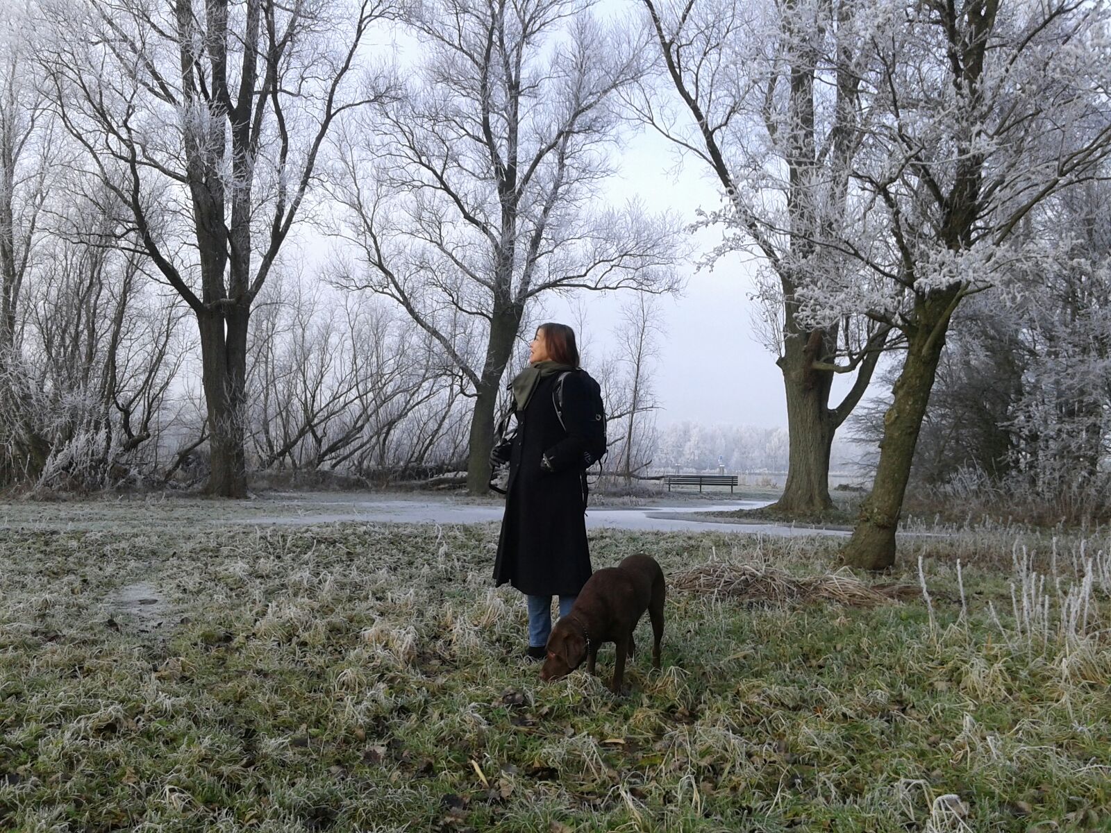 Laura Meddens stands with her guide dog Nugget along the shore with some frosted trees behind her in Amsterdam.