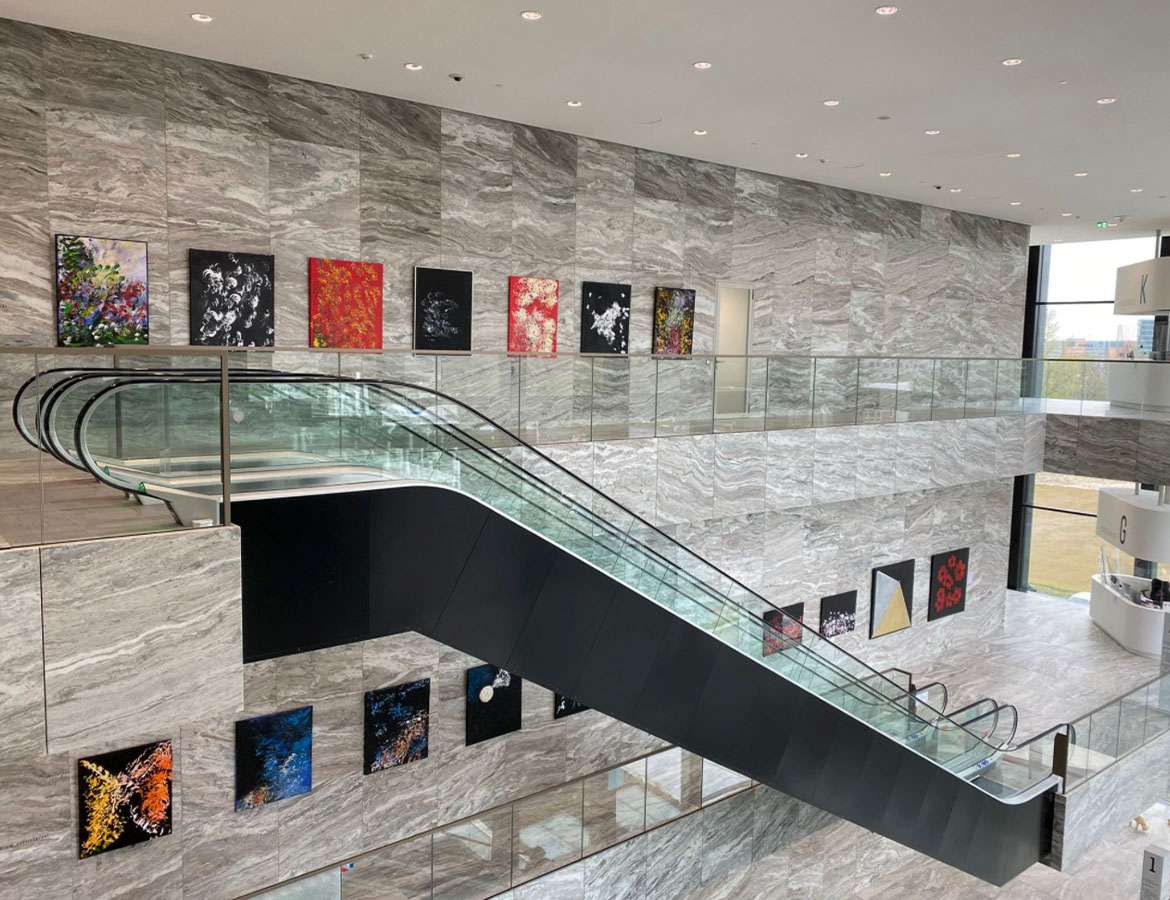 Interior photo of the Rechtbank Amsterdam showing paintings by Laura Meddens displayed on two floors with escalators in the foreground of the open atrium.